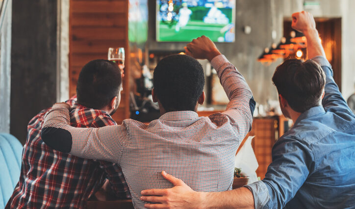 Three men watching football on TV in sport bar, back view