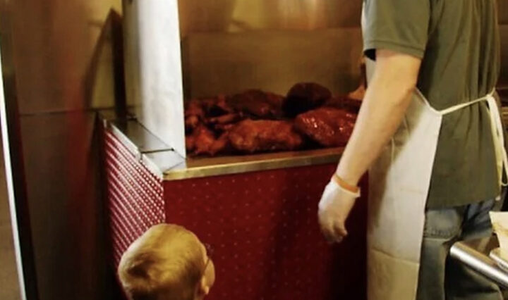 Man standing at grill, barbequing with child.