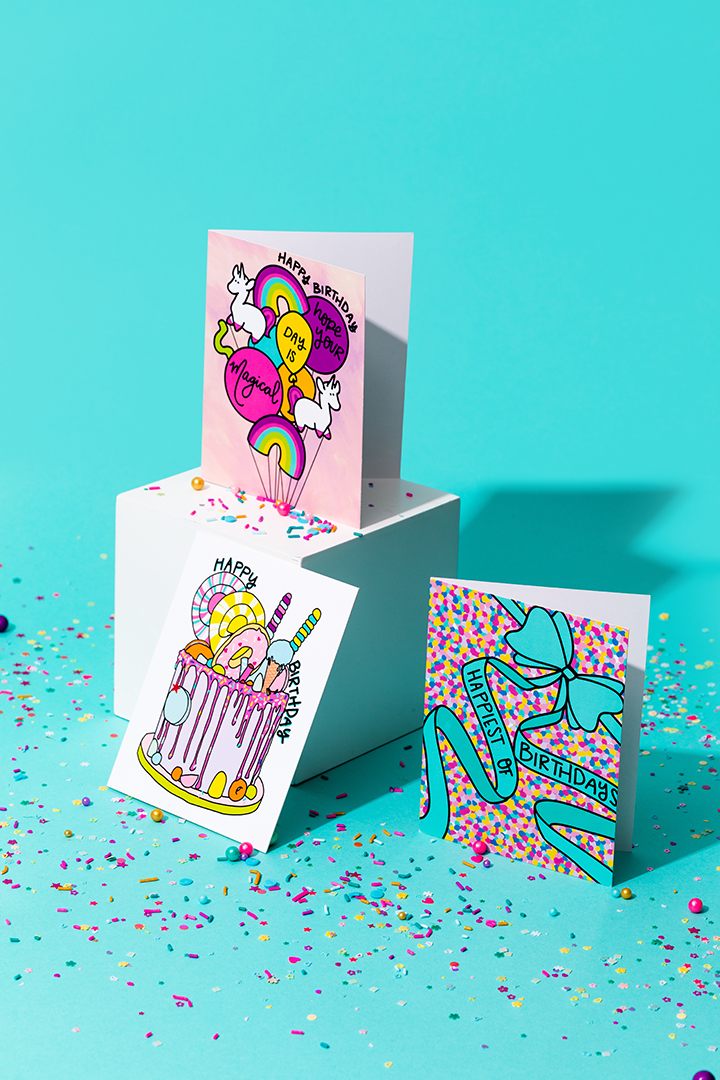 Pretty-Peacock-Paperie - Central Florida Lifestyle Three colorful birthday cards on top of a white box in front of a blue background.