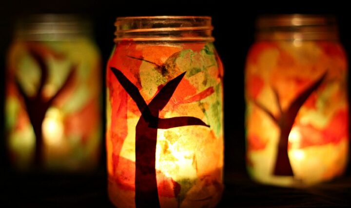 Mason jars decorated with tree branches, colorful tissue paper, and lit candles.
